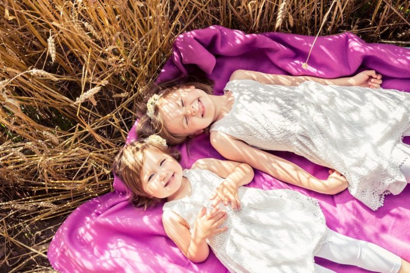 Kinderfotografie von zwei Mädchen draußen auf einer lila Decke.