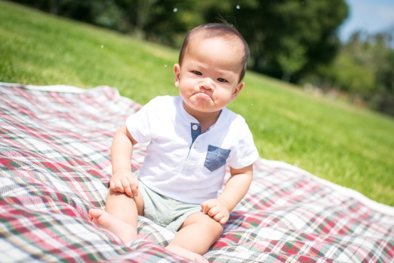 Kinderfotografie von einem kleinen Jungen sitzt schmollend auf einer Picknickdecke.