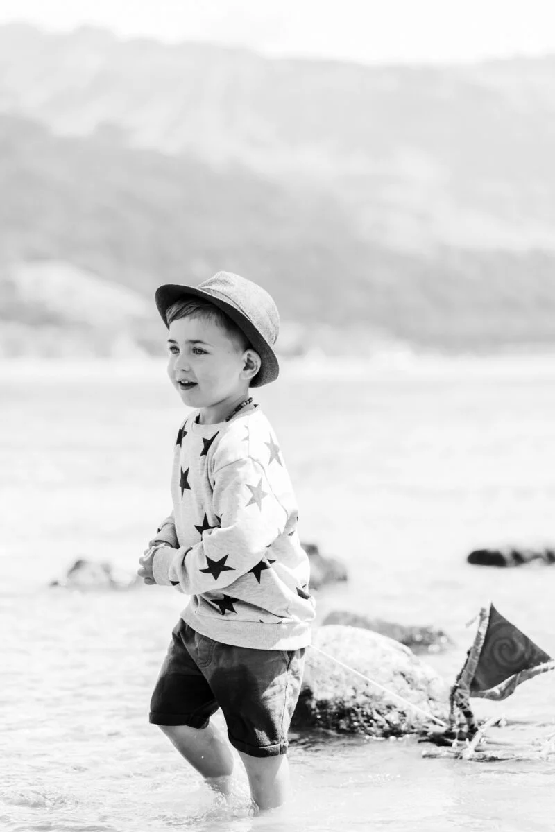 kleiner junge spielt mit holzschiff im wasser